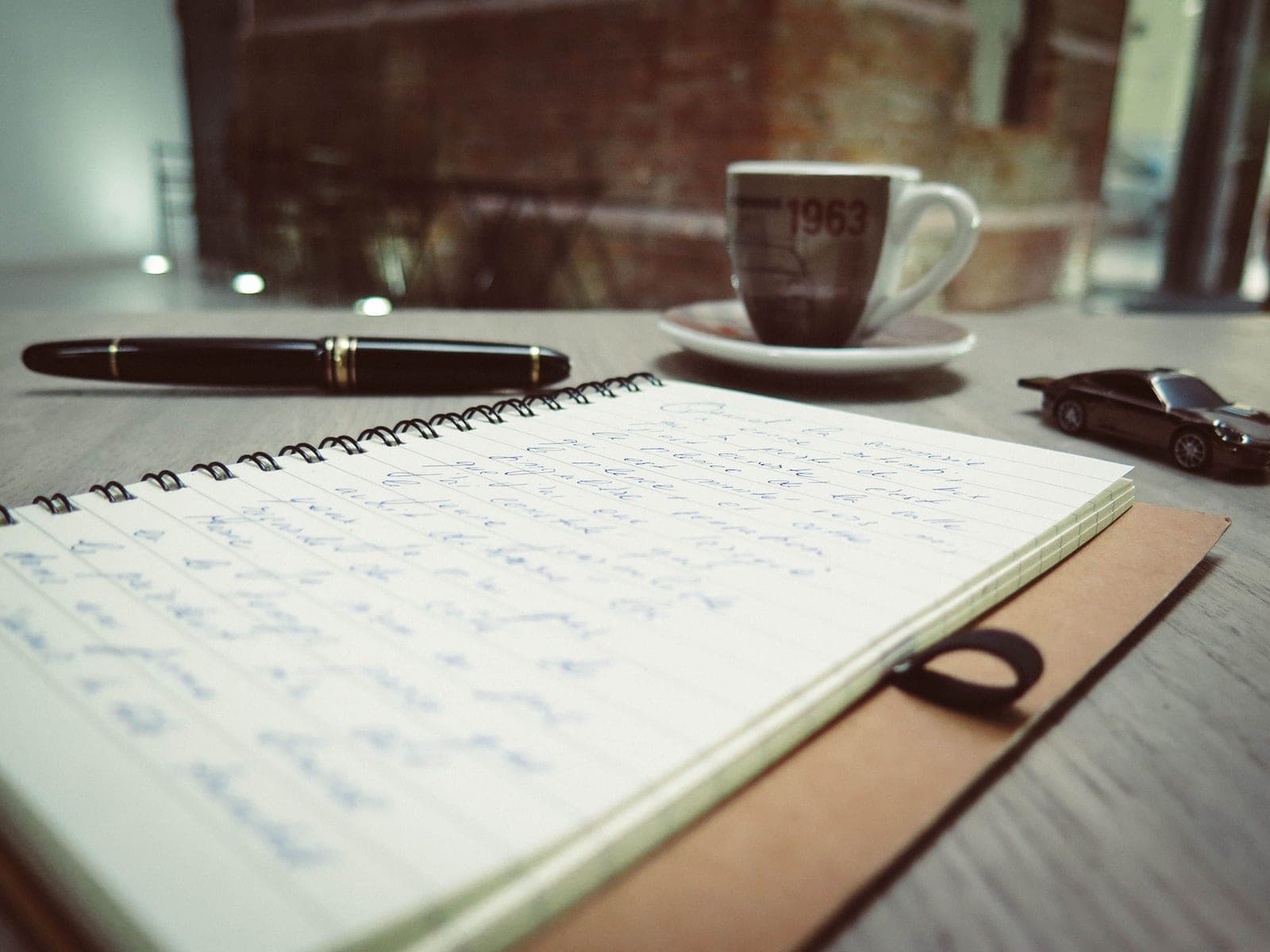 An open notebook and pen on a plain desk beside a mug